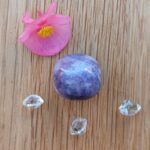 Pink flower, purple polished stone and clear crystals on wood