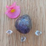Purple polished stone, clear crystals and pink flower on wood