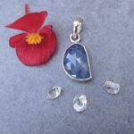 Blue gemstone pendant beside red flower