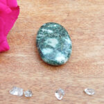 Polished green stone with crystals on wooden surface
