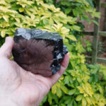 Hand holding large black obsidian stone outdoors