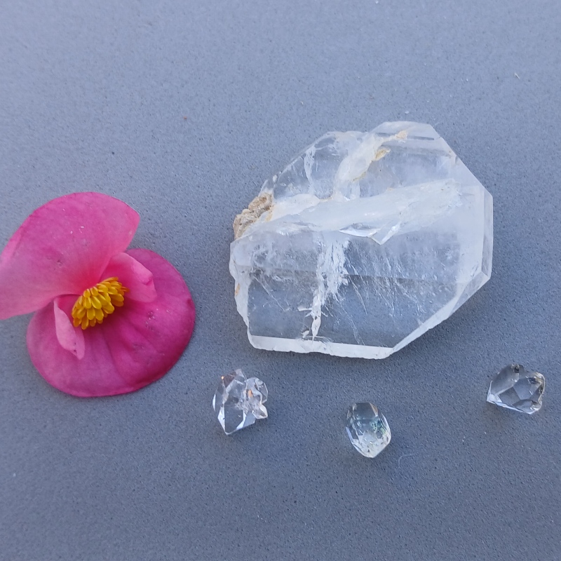 Pink flower beside clear quartz crystals on grey surface