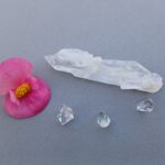 Clear quartz crystals and pink flower on grey surface