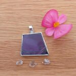 Purple gemstone pendant with pink flower on wood