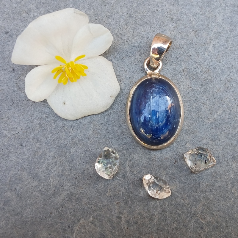 Blue gemstone pendant beside white flower and crystals