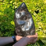 Hands holding polished black stone sculpture outdoors