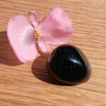 Pink flower beside glossy black stone on wood