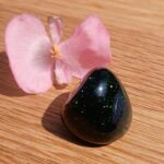 Polished dark green gemstone beside pink flower