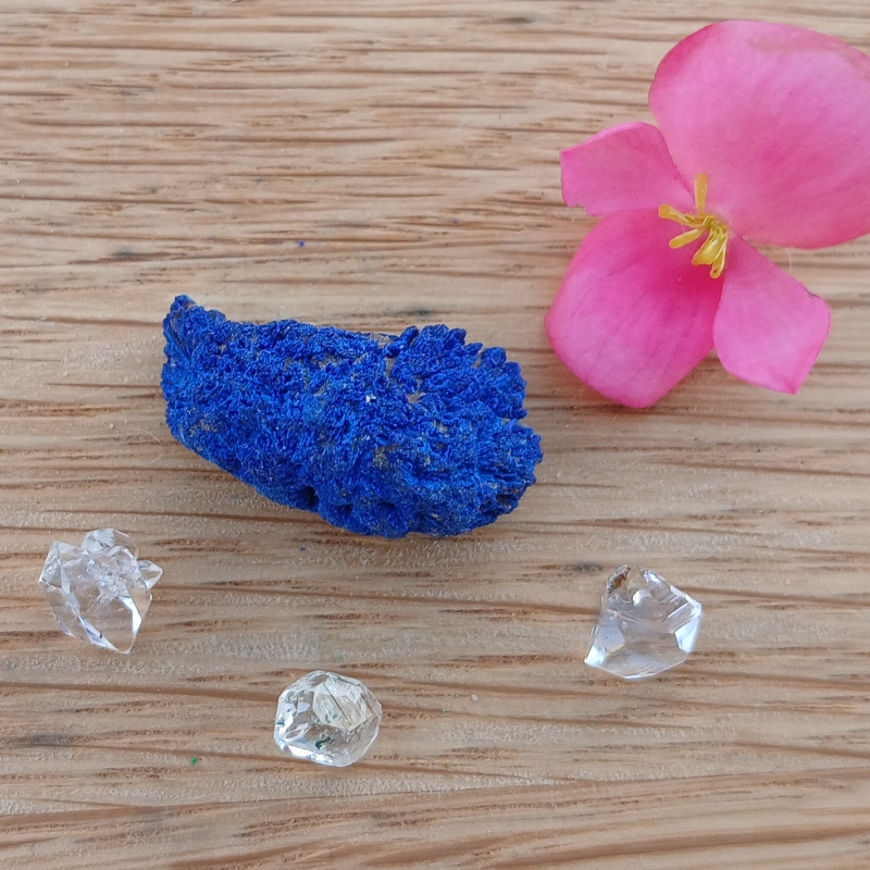 Blue mineral specimen, clear crystals and pink flower on wood