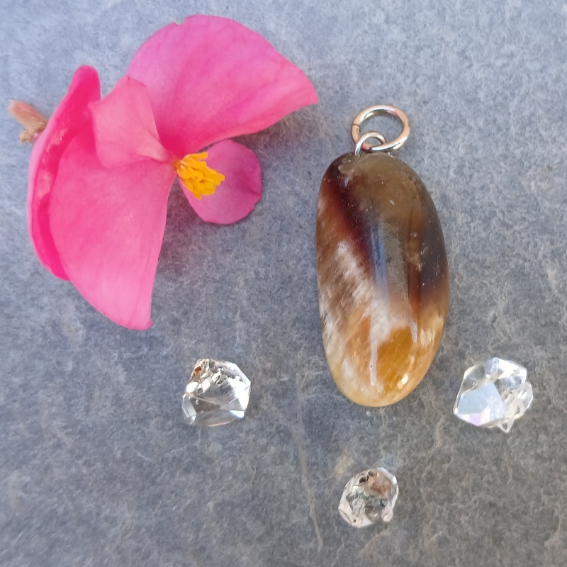Polished brown gemstone pendant beside pink flower and crystals