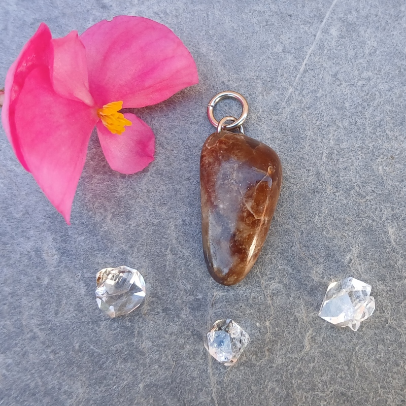 Brown stone pendant beside pink flower and crystals
