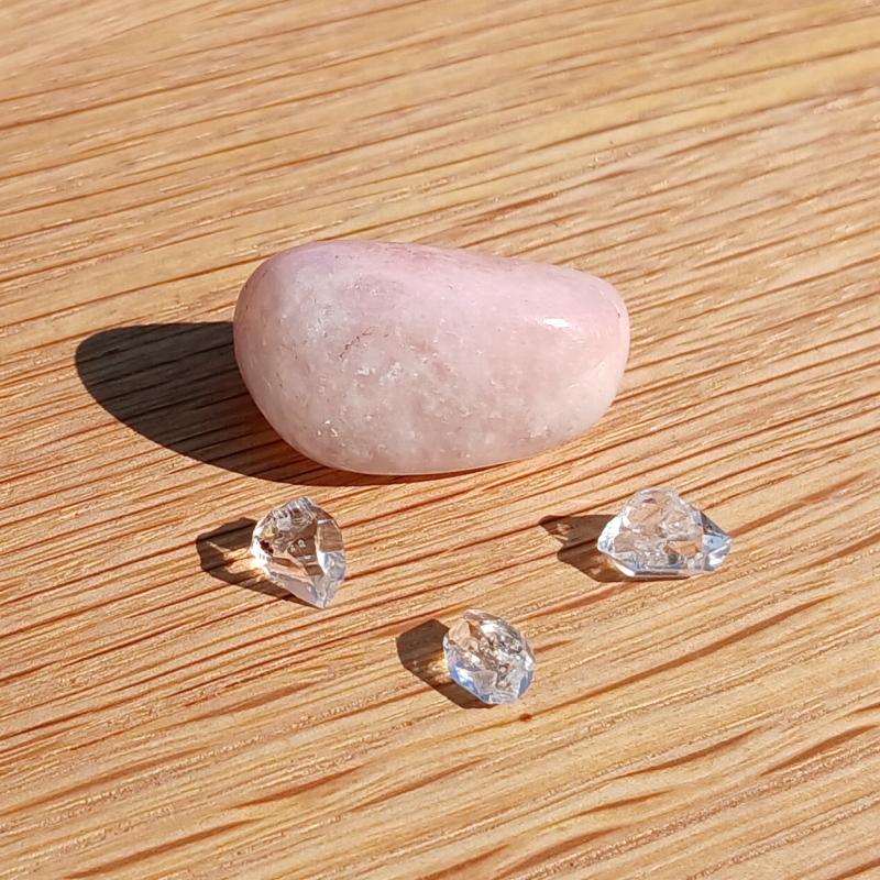 Rose quartz pebble and clear crystals on wooden surface