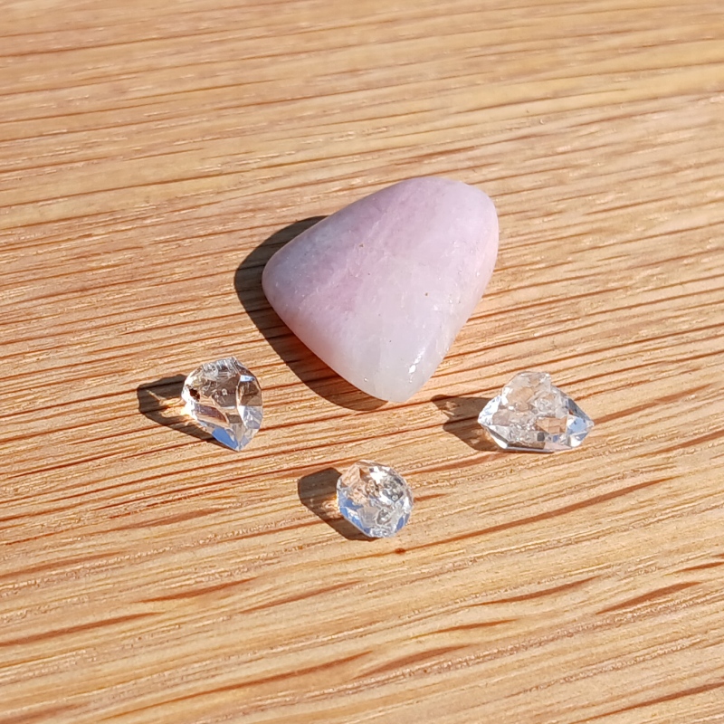 Pink tumbled stone with three clear crystals on wood