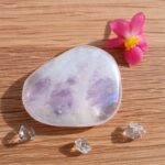 Polished pale purple crystal with pink flower on wood