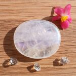 Polished translucent crystal with pink flower on wooden surface