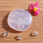 Polished translucent purple crystal with pink flower on wooden surface