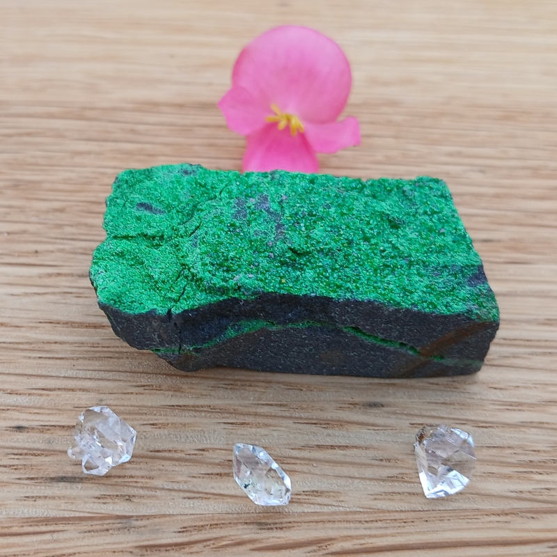 Green mineral specimen with clear crystals and pink flower