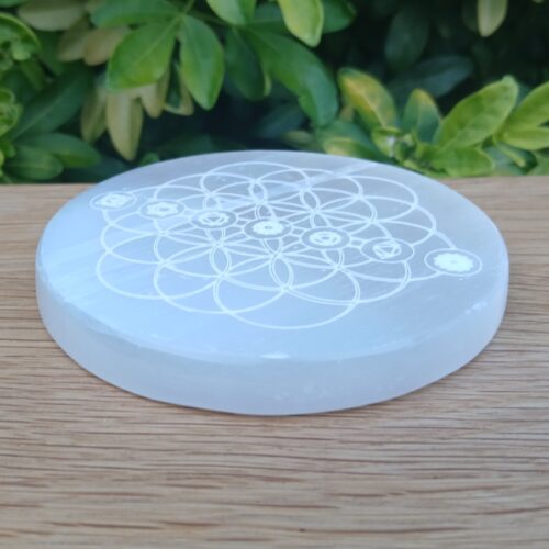 Engraved round selenite crystal plate on wooden surface